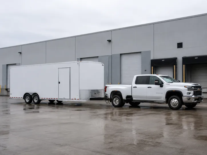 White pickup truck towing a large enclosed trailer outside a warehouse